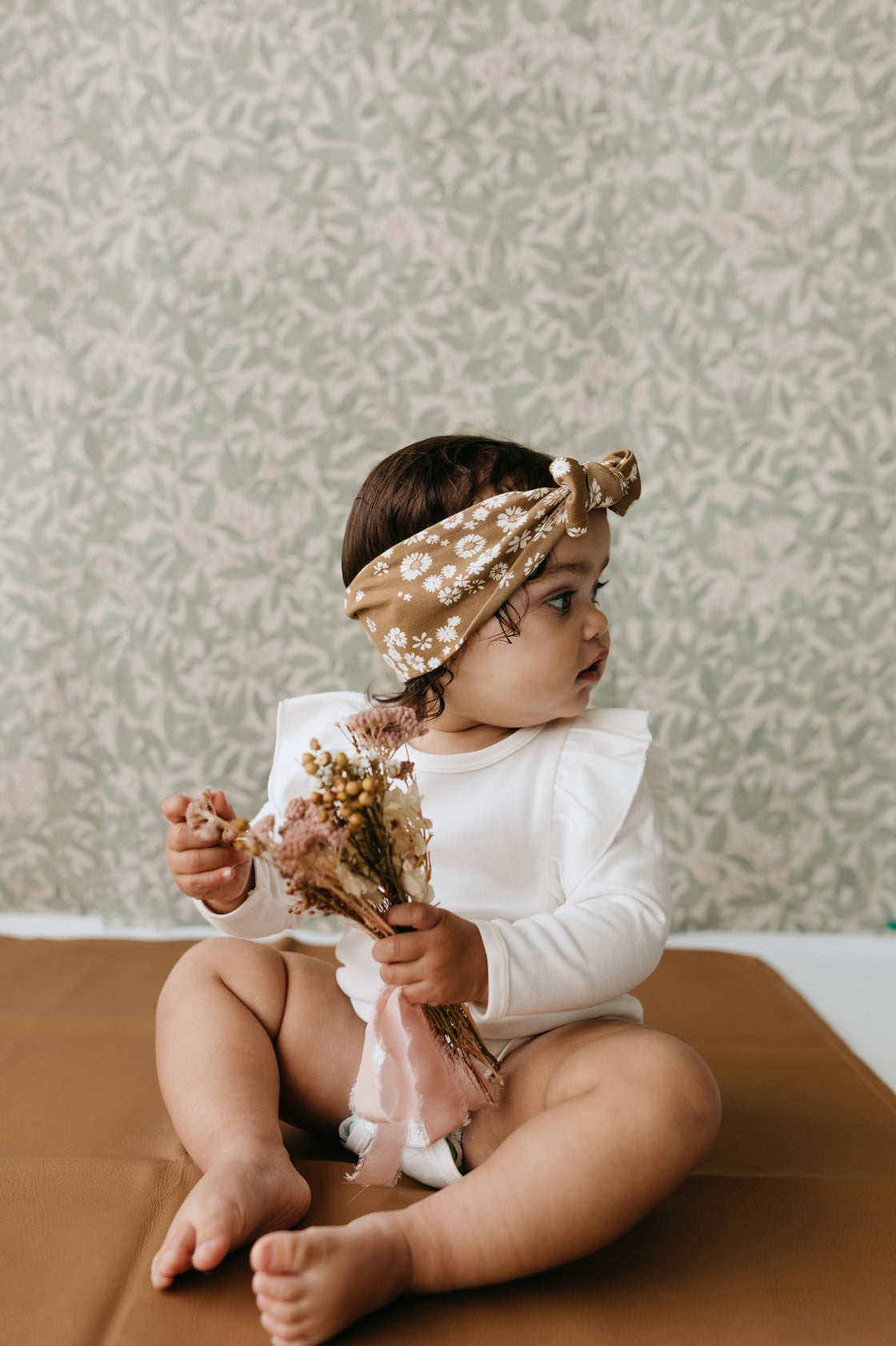 Baby jente med hvit body med puffermer som holder blomster